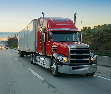 Red semi driving on interstate during sunset